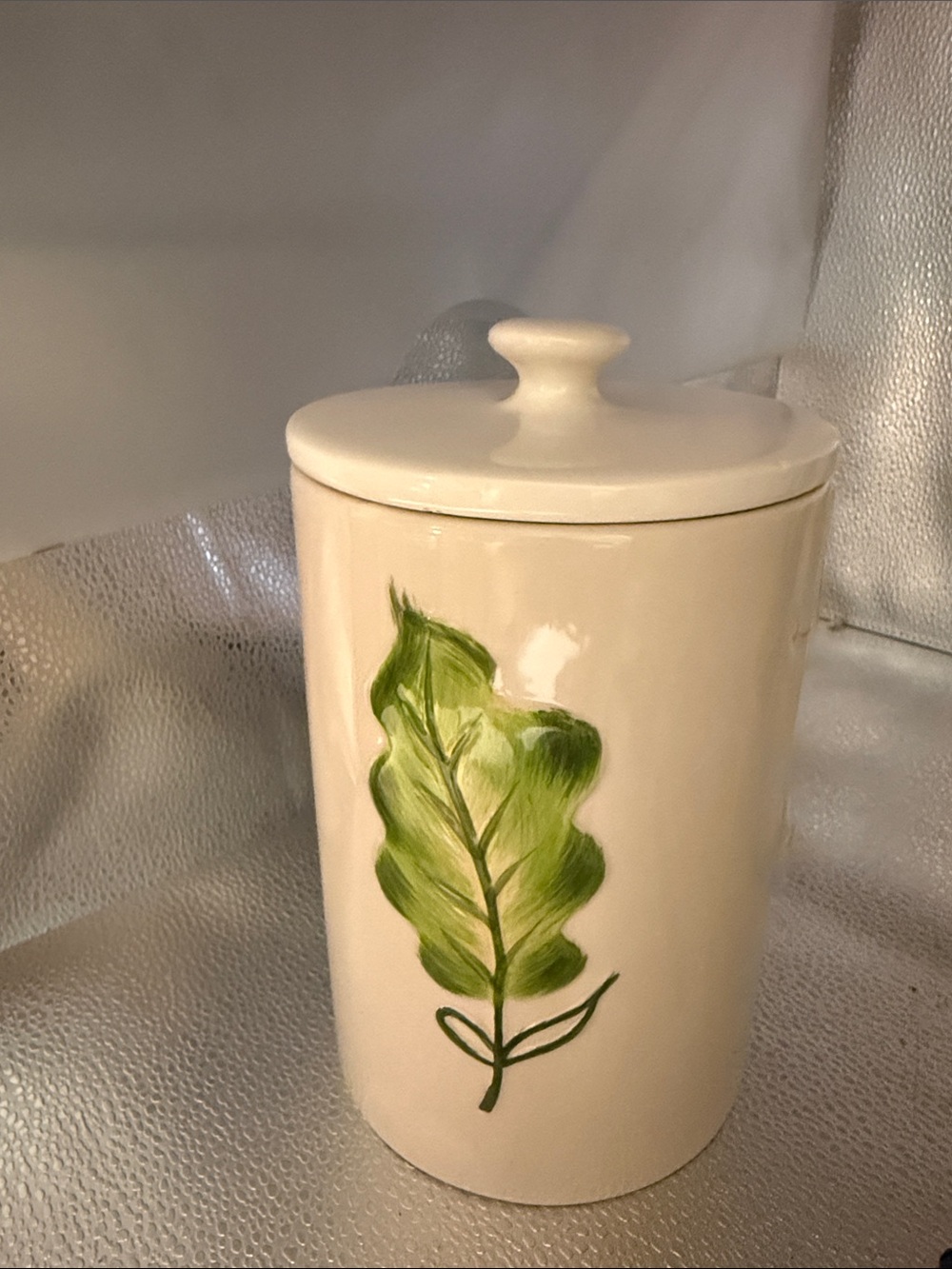 Vintage cylindrical Pier 1 cream canister with a hand painted green leaf